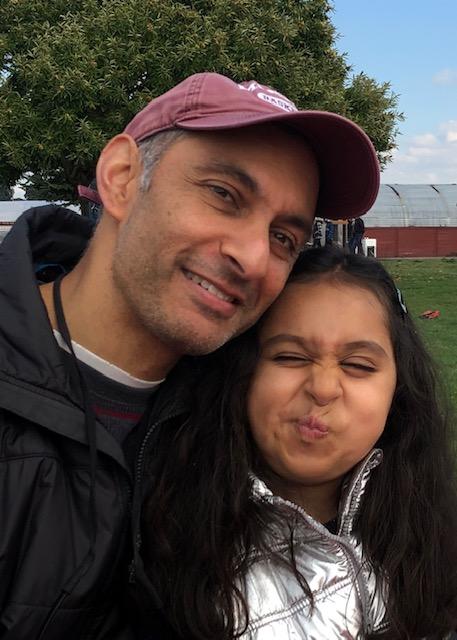 Dahnesh stands smiling next to his daughter Mina. 