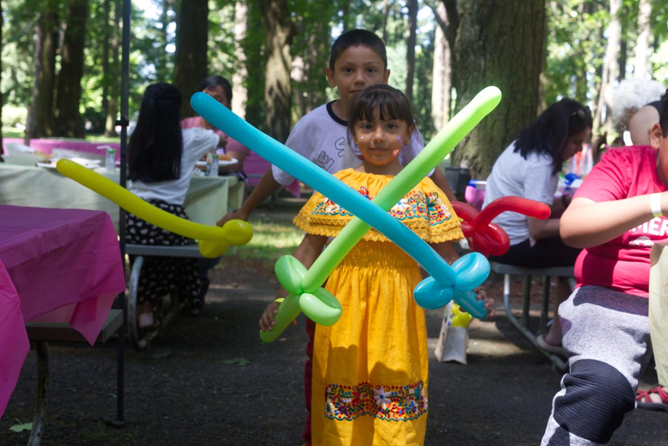 two kids, a little girl wearing a traditional dress holds balloon swords.