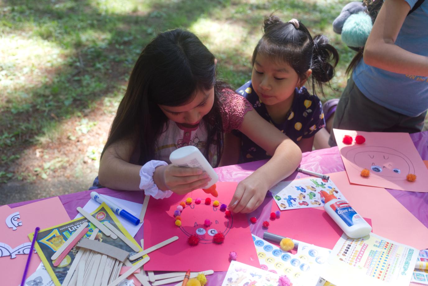 two little girls glue multicolor circles on an owl at the arts and craft table