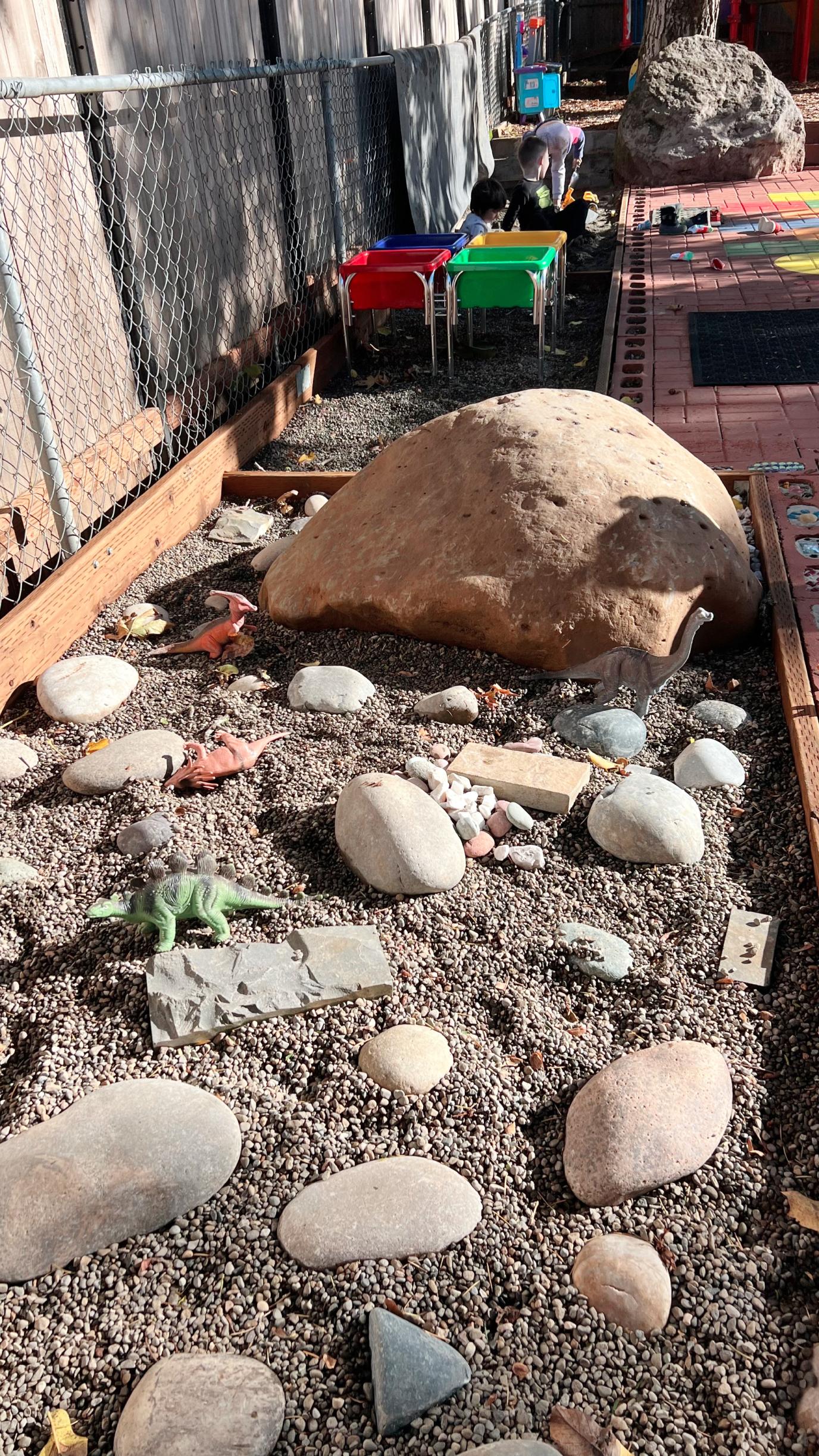 Colorful playbox filled with sand, rocks, and toy dinosaurs, at Yuri’s Childcare