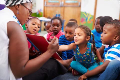 A preschool teacher showing a book to a group of engaged preschoolers