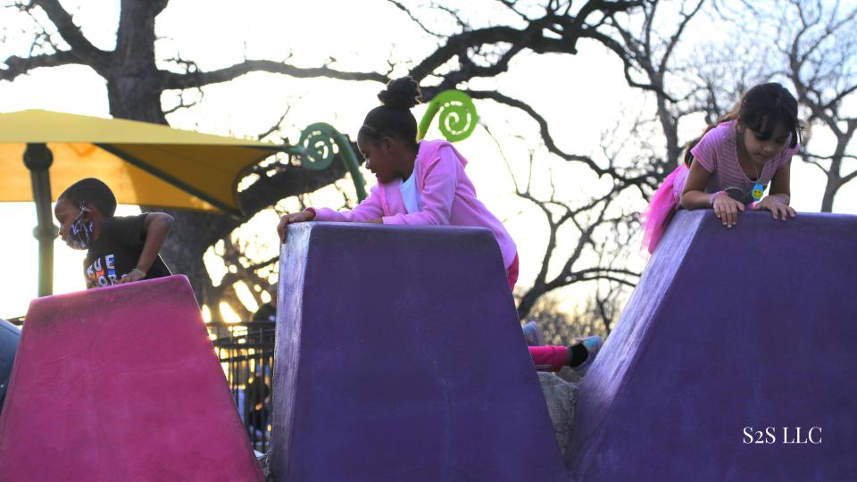 3 children playing on a multi-colored play structure 